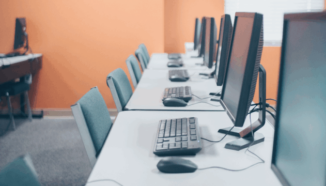 Netjes ingericht computerlokaal met een rij desktopcomputers, toetsenborden en muizen op witte tafels, klaar voor digitaal onderwijs of examens.